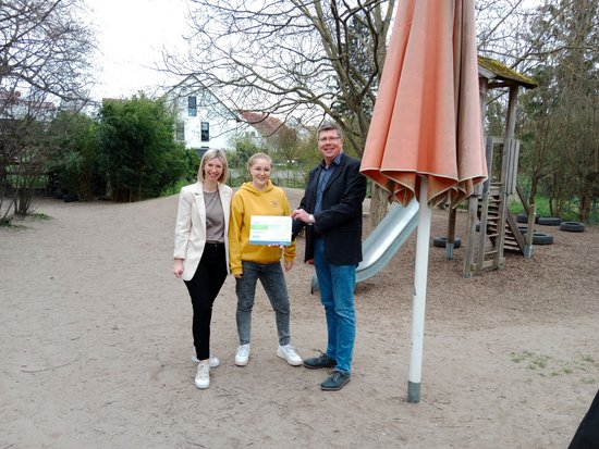 Drei Personen bei der Preisübergabe im Außengelände der Kita.